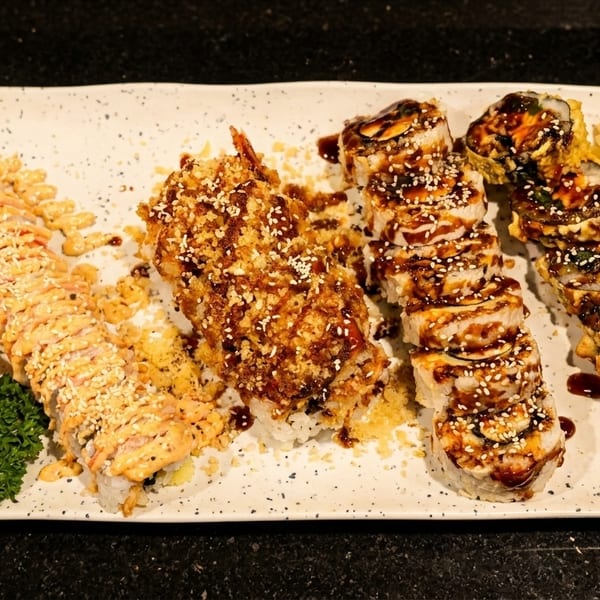 Four different sushi rolls, garnished with orange, cherry, and parsley, on a white rectangular plate.